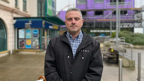 A man wearing a coat outside a shopping centre.