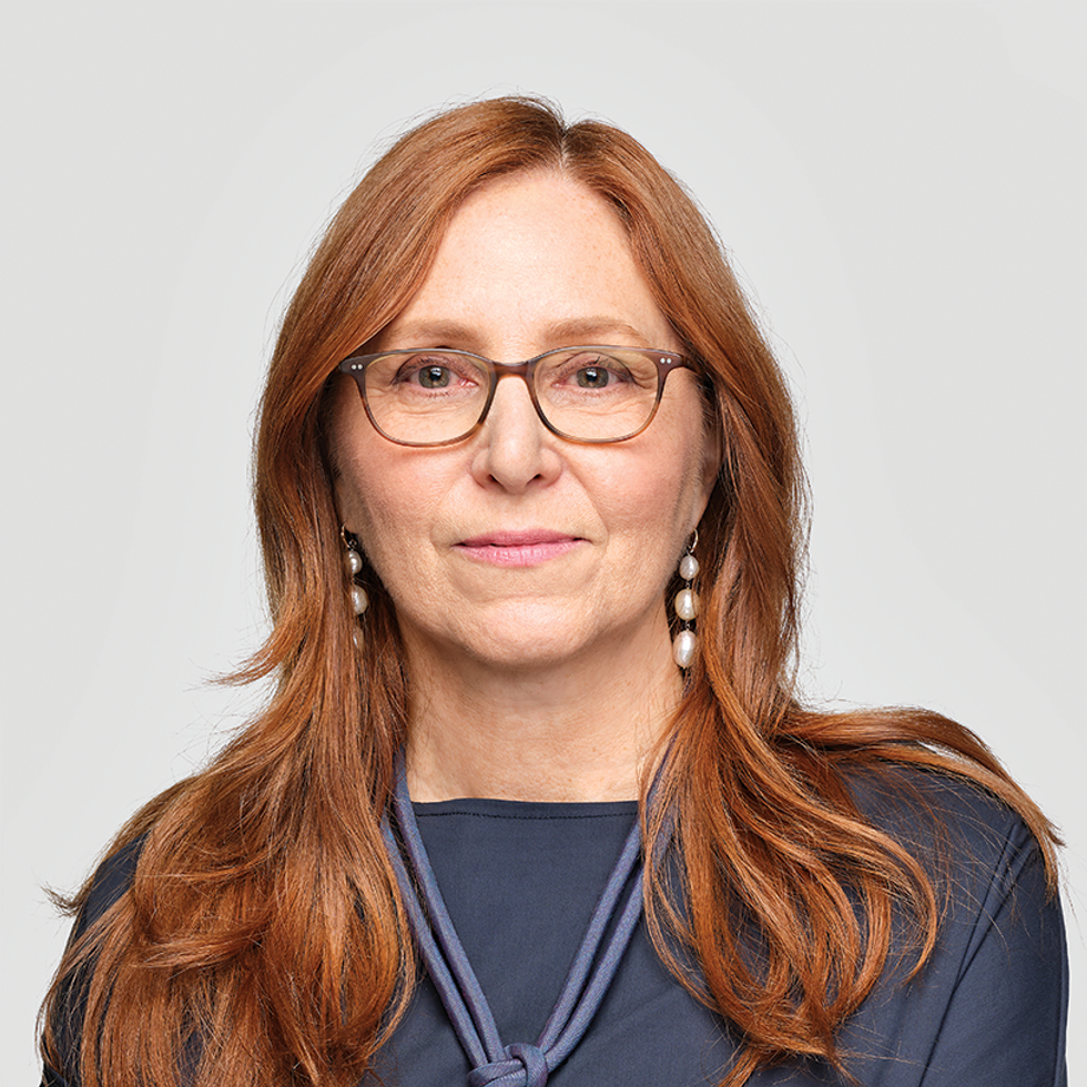 A woman with long, reddish-brown hair wearing a dark shirt and knotted scarf.