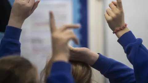 PA Media A generic image of unidentified primary school pupils holding their hands up while wearing blue sweatshirts.