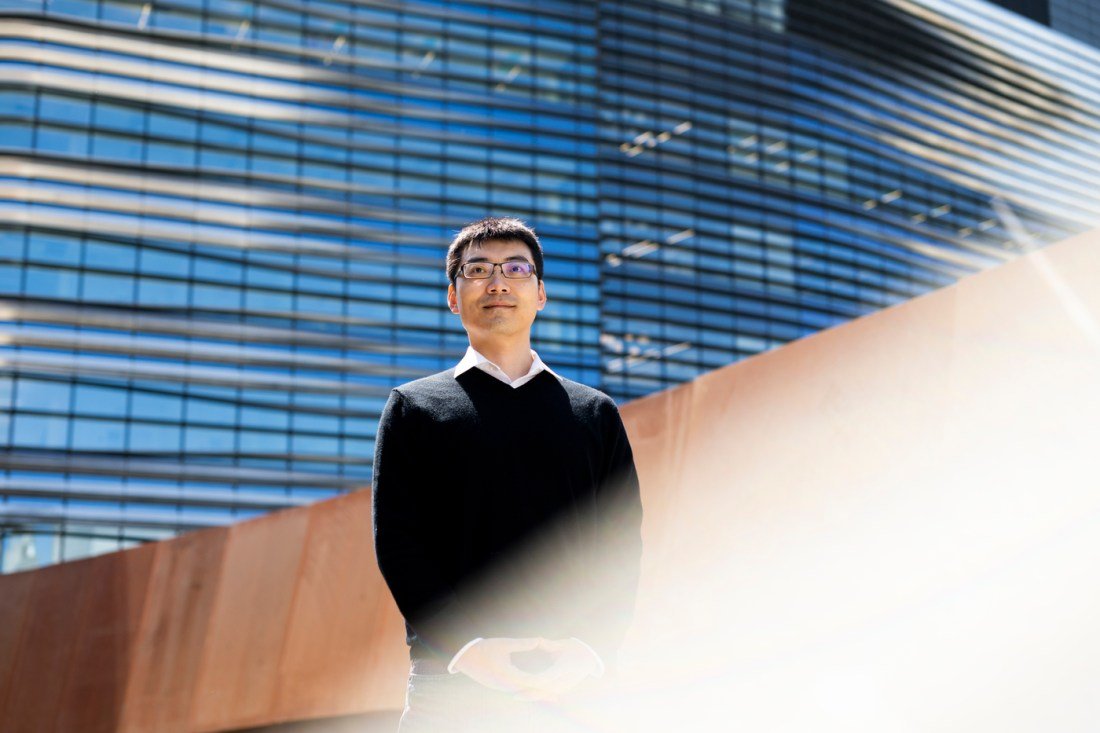 Portrait of Dakuo Wang standing outside in front of a modern building.