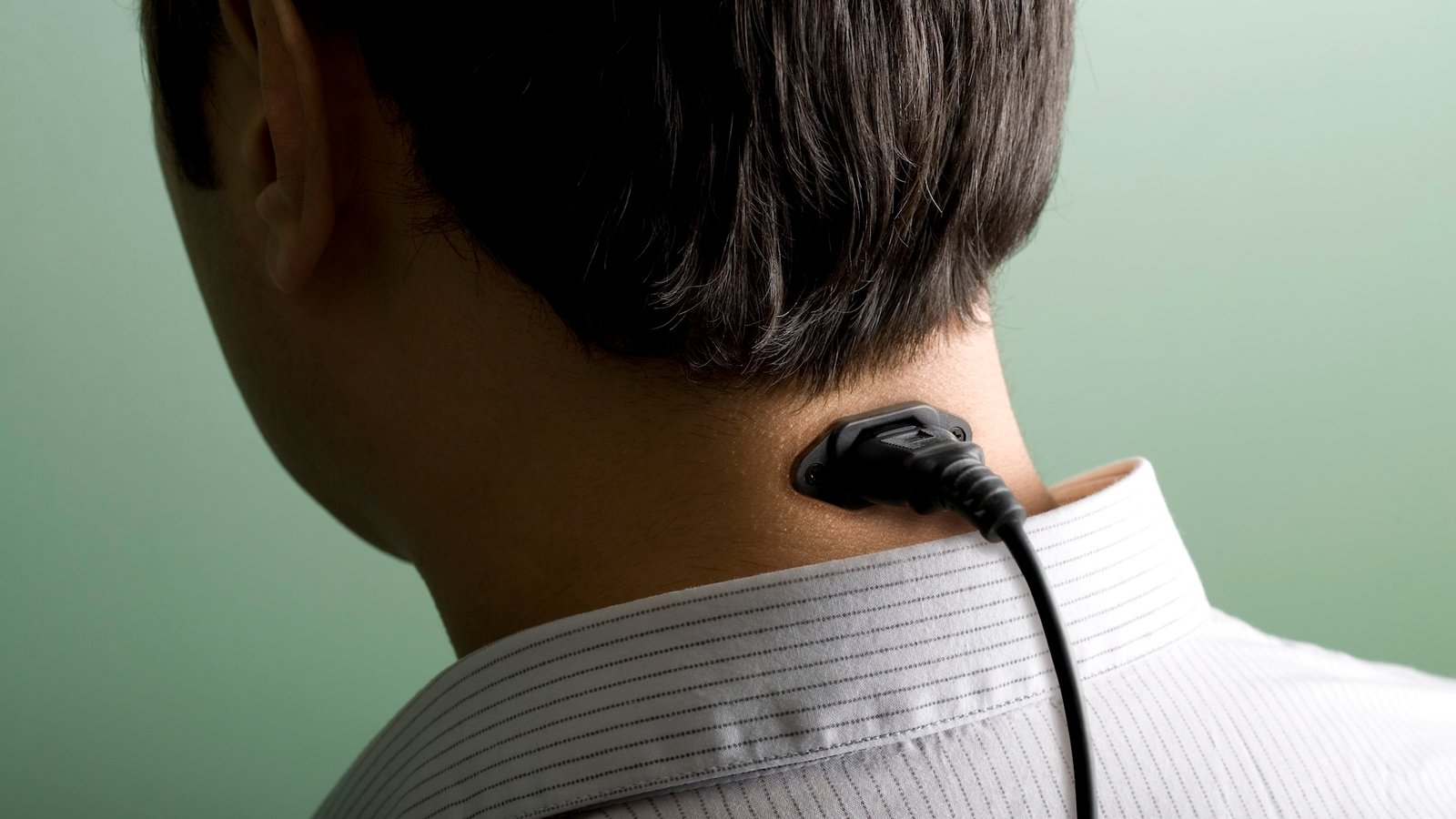 a digitally-manipulated image showing the back of a businessman's head with a power cable in his neck 