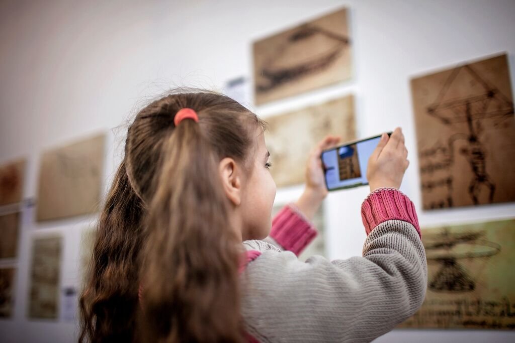 Curious girl exploring a contemporary art exhibition with augmented reality mobile application, future technology in everyday life, indoor lifestyle