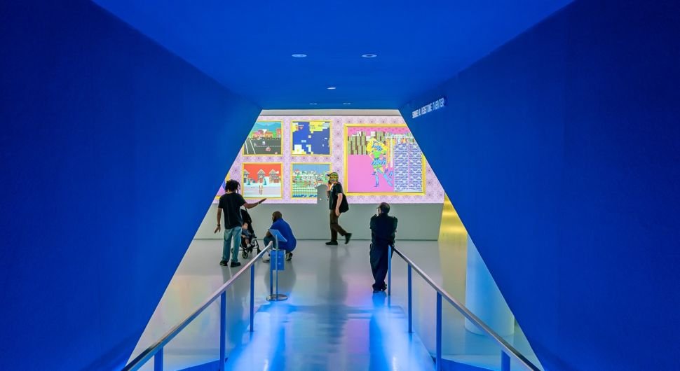 Visitors view colorful digital artworks on display in a vivid blue gallery space at the Museum of the Moving Image in New York